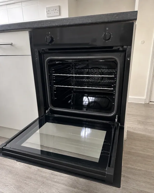 A built-in oven with the door open after an end of tenancy clean, racks back in place and the glass polished