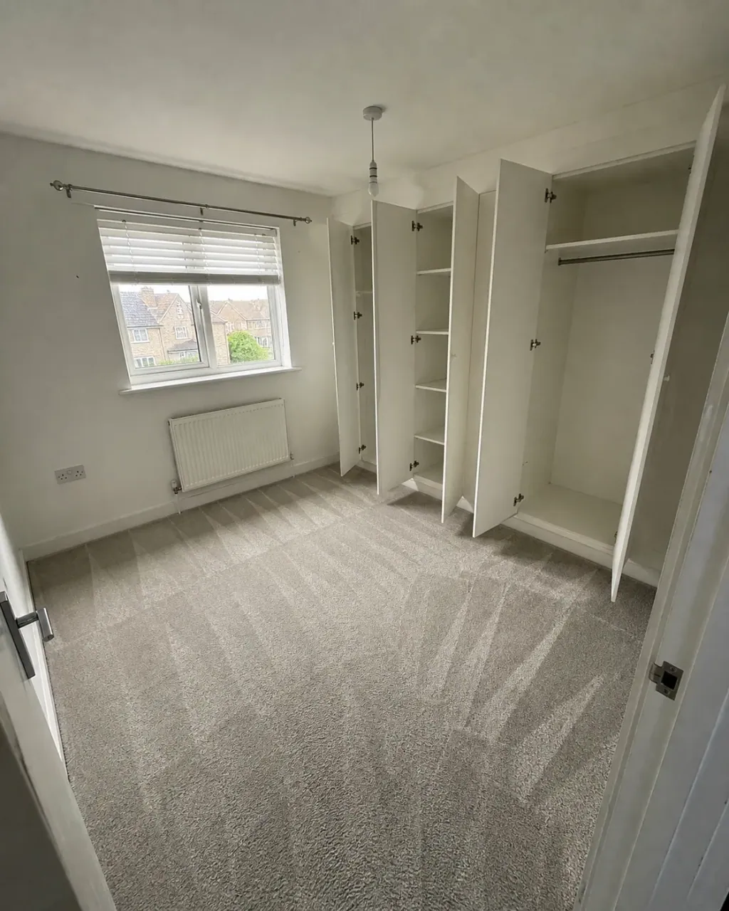 An empty bedroom, fitted wardrobes open on bare shelves and rails after checkout